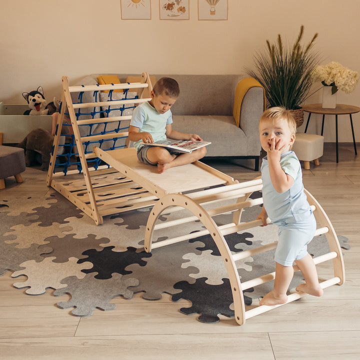 Children playing on a wooden indoor climbing set, which includes a slide and a triangular climbing structure and arch, made from wood