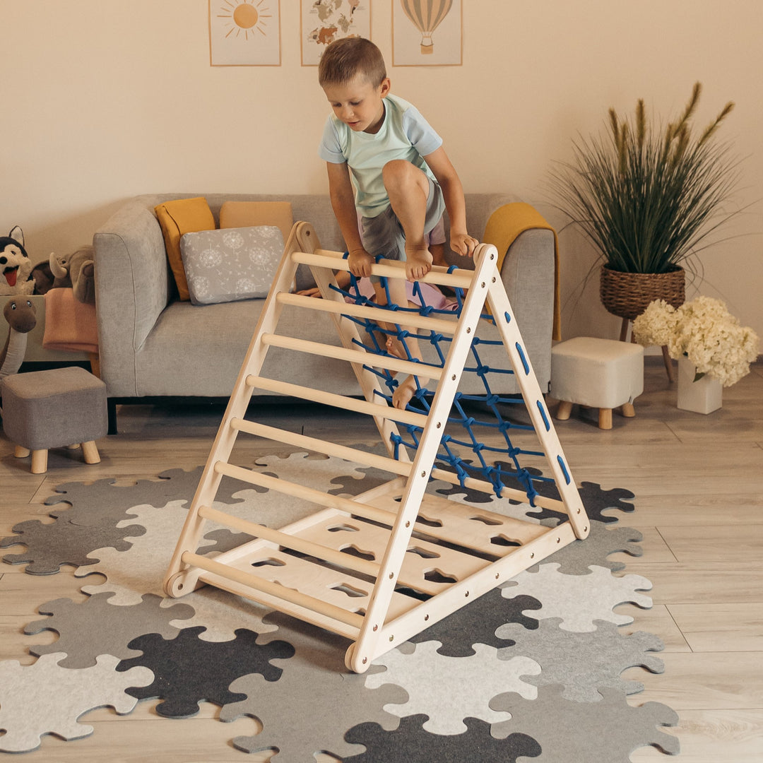 A child climbing up a wooden climbing triangle with 3 different sides, rope net side, ladder side, climbing side. 
Climbuptoys