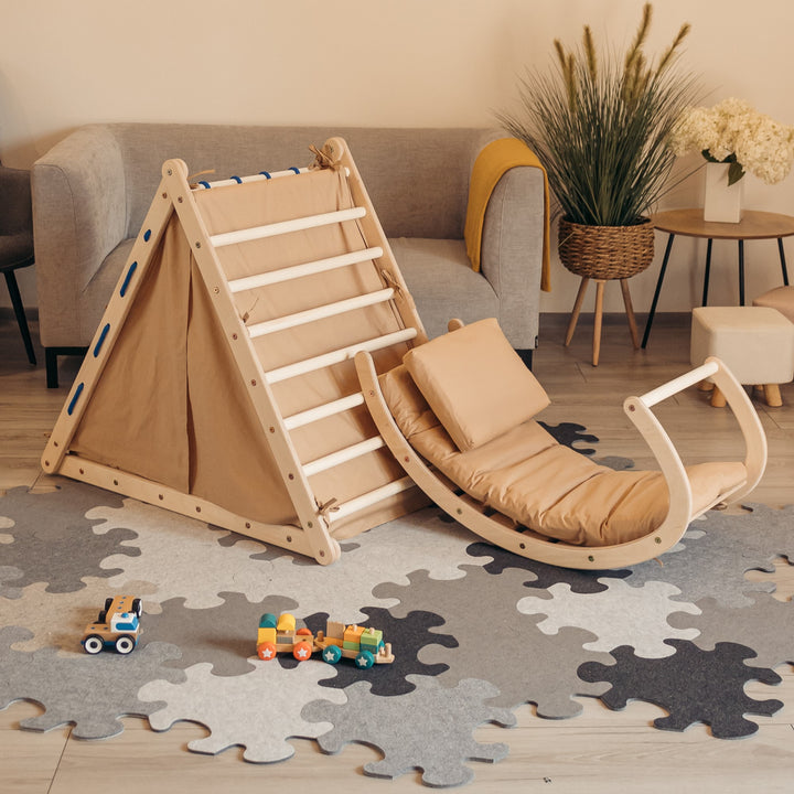 Children's climbing set with accessories including a slide, a tent, and a rocking toy, all in brown color, set in a room with a grey floor mat.